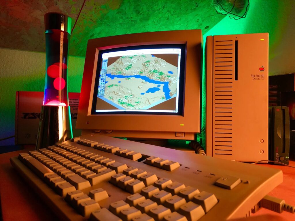 A Macintosh Quadra 700 displaying the game SimCity 2000, sitting on a desk next to a lava lamp.