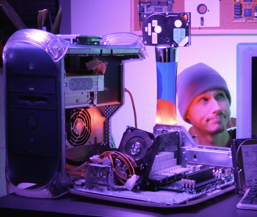 Chris wearing a beanie while crouched behind a desk which holds a partially disassembled Power Mac G4.